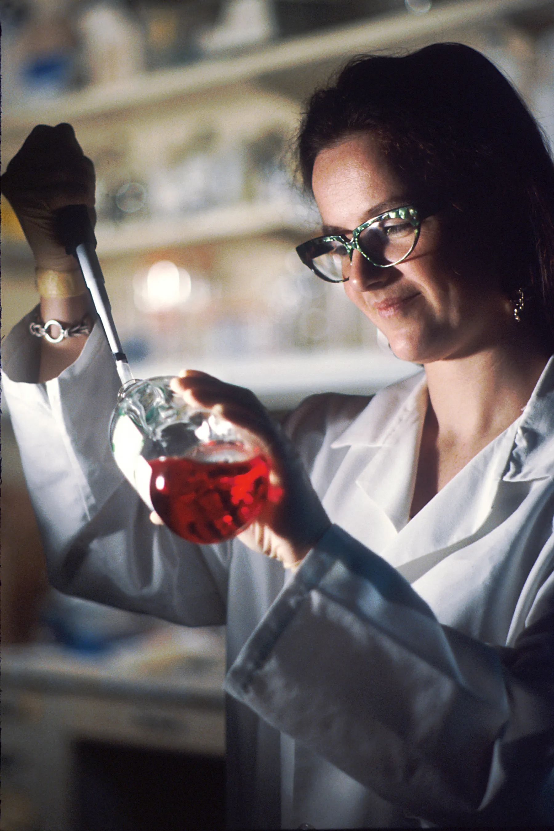 A researcher holds up a flask of red culture medium to the light.